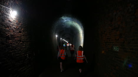 group of people walking through a dark brick tunnel