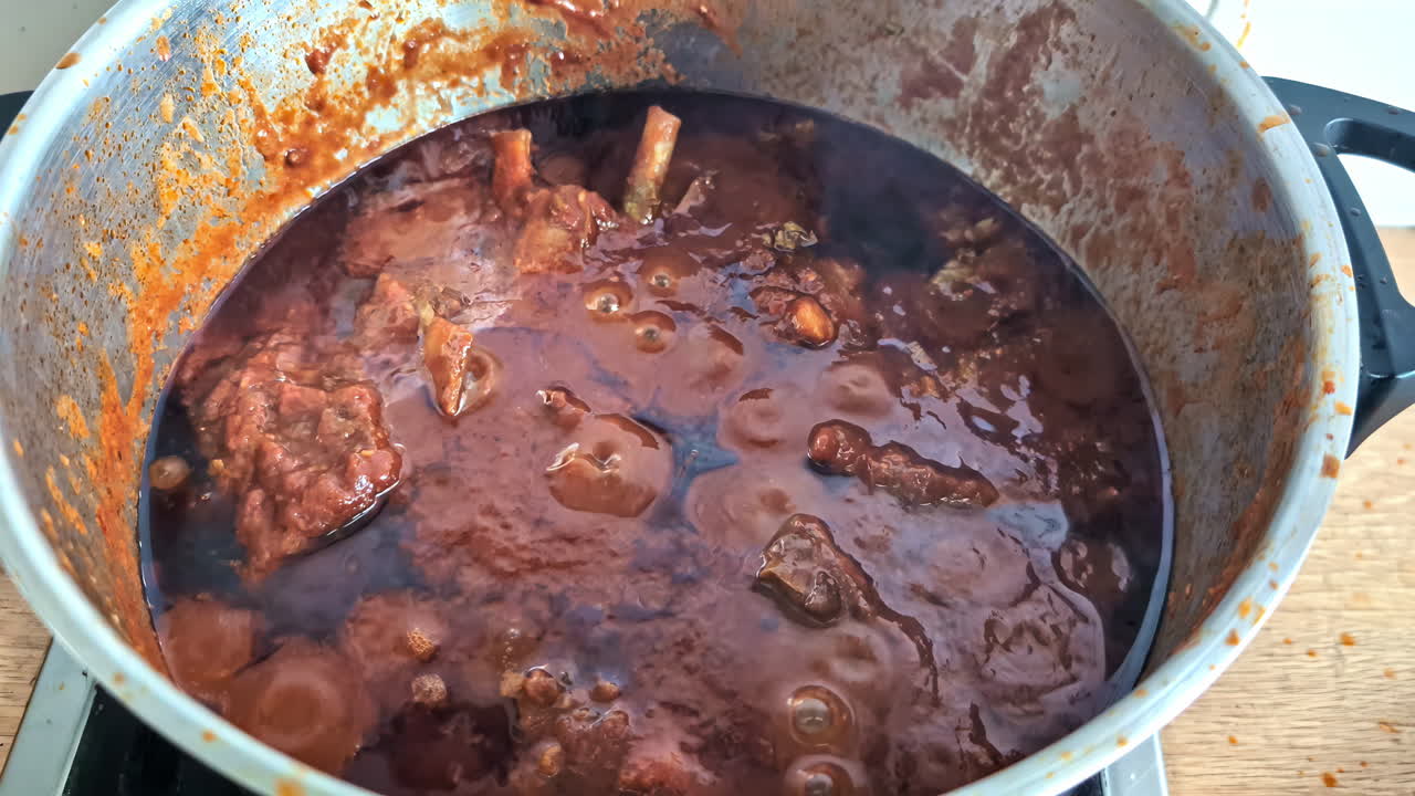 un guiso rico hierve en una gran olla de metal con trozos de carne visibles en el caldo burbujeante
