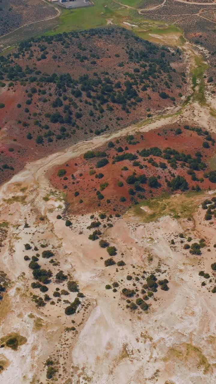 Diverse colors of dry landscape with scarce greenery. Some cabins and roads at backdrop. Aerial perspective. Vertical video