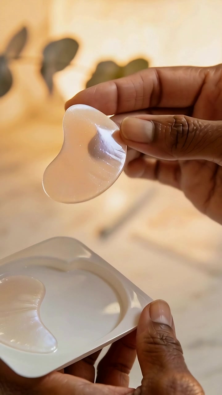 Vertical video: Pressing peeling hands lifting hydrogel eye patch on vanity tray, rotating to apply