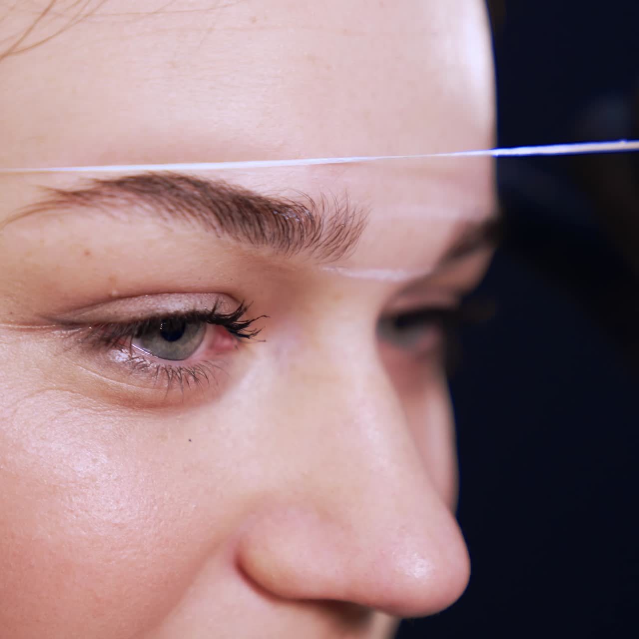 Marking the lines for the future brow line with the help of a thread. White lines are drawn on the forehead of a client. Extreme close up