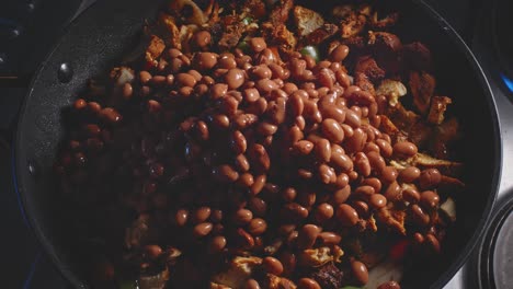 adding drained canned beans into spicy chicken breast cooking in a pan