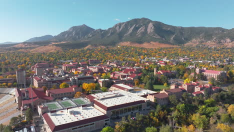 aerial view of cu boulder campus and folsom football field surrounded by green and yellow fall trees with the rocky flatiron mountains in the background in the front range of colorado panning left