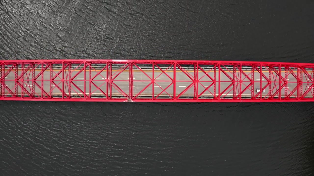 Vista aerea dall'alto del ponte ad arco in acciaio rosso AMVETS Memorial Bridge sopra la diga di New Croton in una giornata di sole. La telecamera, inclinata direttamente verso il basso, ha eseguito un dolly in sopra il ponte mentre i veicoli passano
