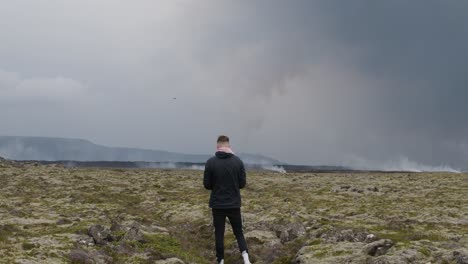 un hombre despega y vuela un dron cerca del volcán grindavik en el cráter sundhnúkur, islandia, con el volcán en erupción en el fondo