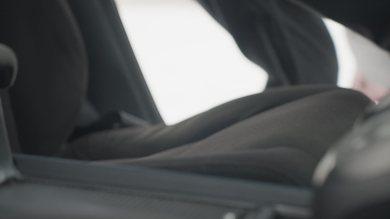 close up interior view of car seat with open door as person enters and sits down, daylight visible through open doorway, fabric seat texture clearly seen