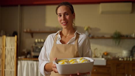 una mujer sonriendo a la cámara, sosteniendo una bandeja de productos horneados.
