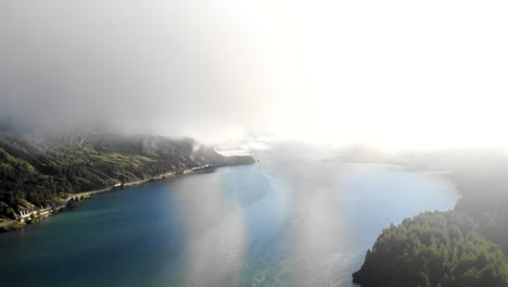 An-early-morning-aerial-flyover-through-the-clouds-over-Lake-Sils-in-Maloja,-Switzerland-with-a-view-of-the-peaks-of-Engadin