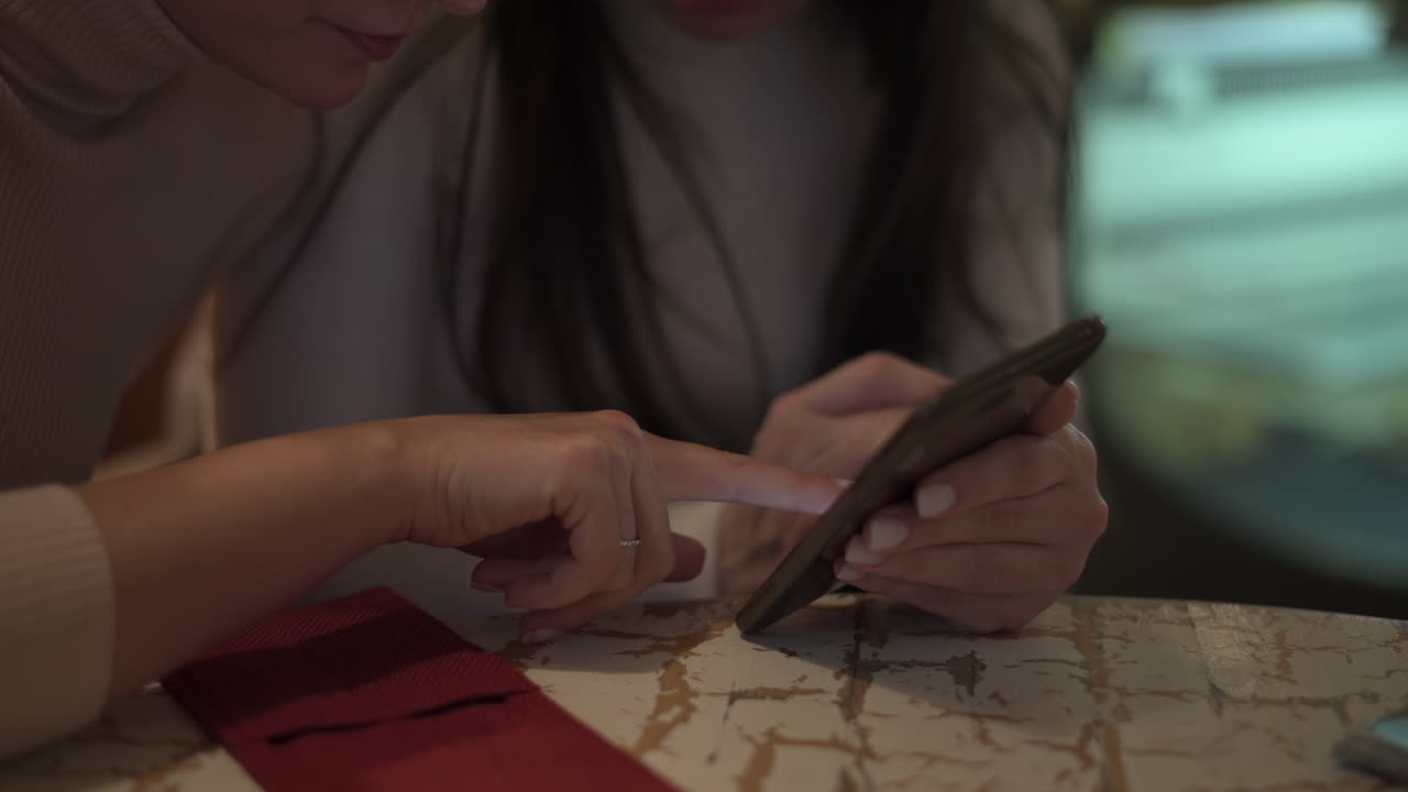 Close up of two women looking at a phone at a table at a cafe