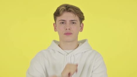 young man showing no sign by arm gesture on yellow background