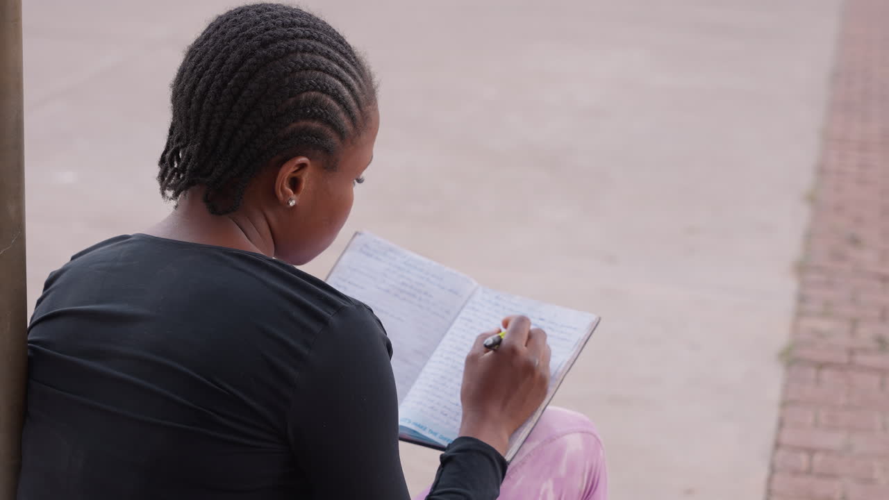 young woman reviewing notes on sidewalk calm, back view with braided hair, pen in hand, steady pacing through page, casual posture, quiet urban study scene, reflective completion