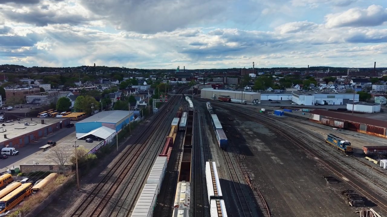 Forward drone fly over debris trains line the tracks in a bustling urban industrial area under cloudy sky, Lawrence, Massachusetts, US