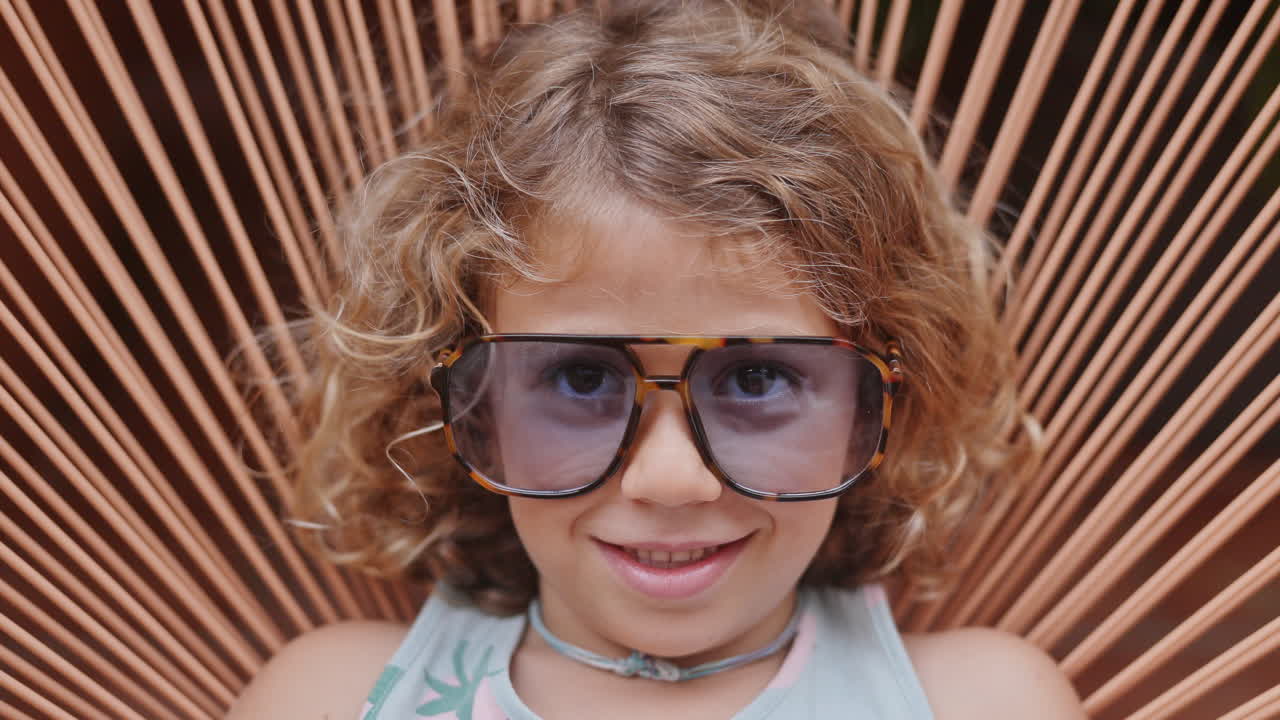 Cool little girl in a garden chair with sunglasses making faces