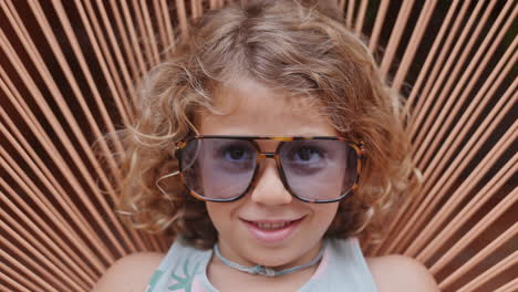 cool little girl in a garden chair with sunglasses making faces