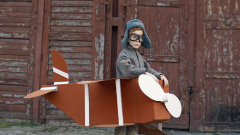 Portrait-Of-A-Cute-Little-Red-Haired-Boy-In-Hat-And-Glasses-Standing-In-A-Cardboard-Plane-And-Smiling-At-The-Camera-1