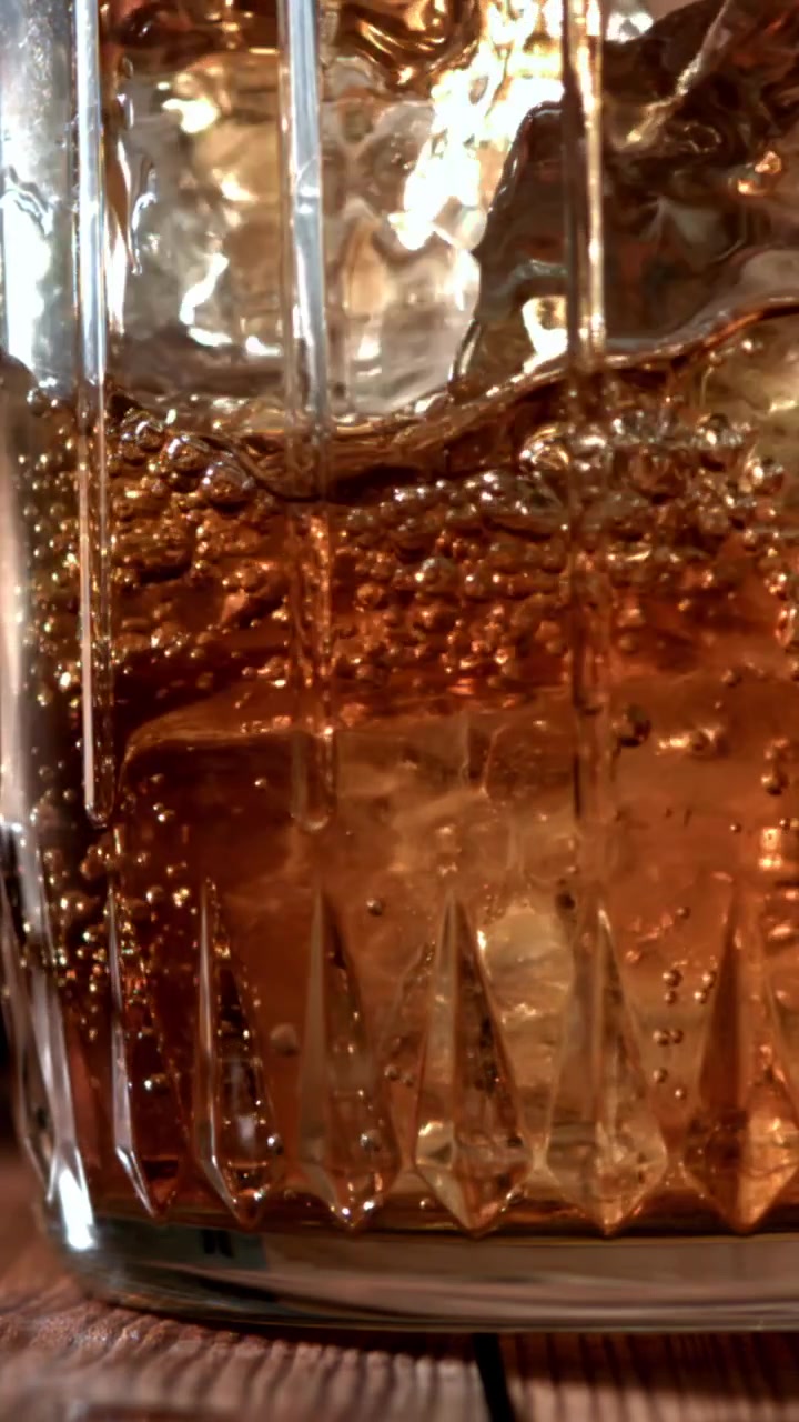 Primo piano di whisky versato su ghiaccio in un bicchiere di cristallo