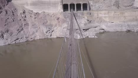 Aerial-view:-Crossing-muddy-river-on-narrow-suspension-foot-bridge