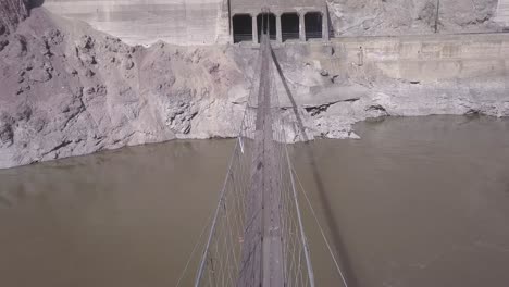 vista aérea: cruzar el río fangoso en un estrecho puente peatonal colgante