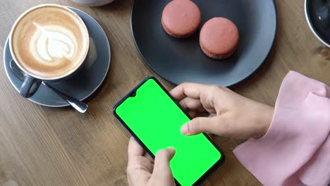 woman using phone at a cafe with coffee and macarons