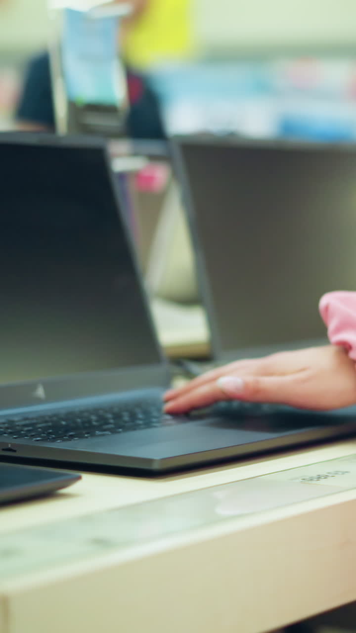 vista del cuerpo de la dama en tela rosada con bolso negro interactuando con una computadora portátil en exhibición en una tienda electrónica, la pantalla de la computadora portable está en blanco mientras la opera, con otras computadoras portátiles ordenadamente alineadas