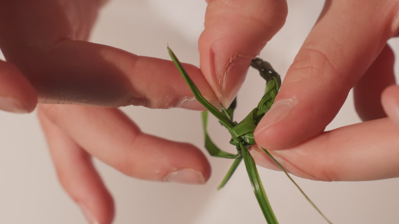 Caucasian hands forming delicate grass knot keepsake, intense closeup of meticulous fingers weaving tiny loop, heirloom feel with family and marriage symbolism, soft warm light, meditative careful
