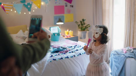 happy little girl playing dress up in bedroom with mother taking photo using smartphone sharing on social media