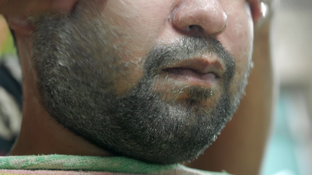 Close-up of a man's bearded face being groomed