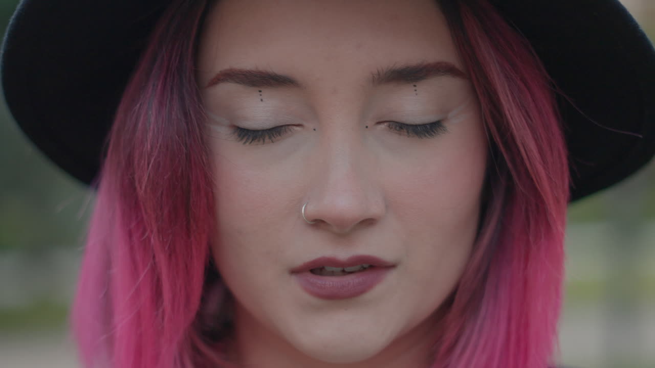 Close-up portrait of a woman with pink hair and a hat
