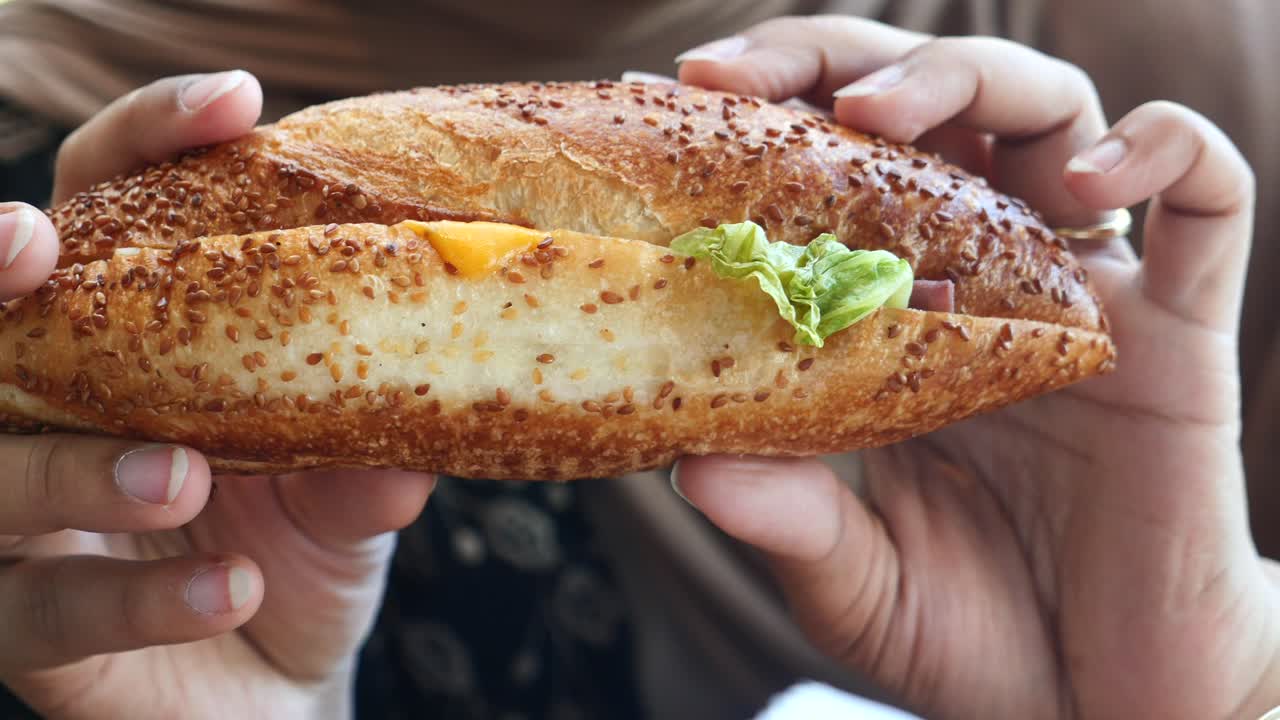 Hands holding a sesame seed baguette sandwich