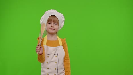 little girl in chef hat and apron holding a whisk, smiling at the camera