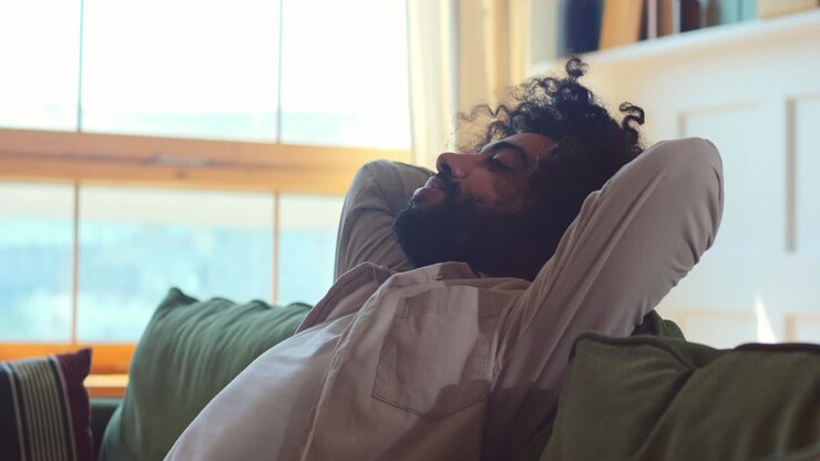 Young selfsatisfied arabian man falls on sofa leaning back in living room