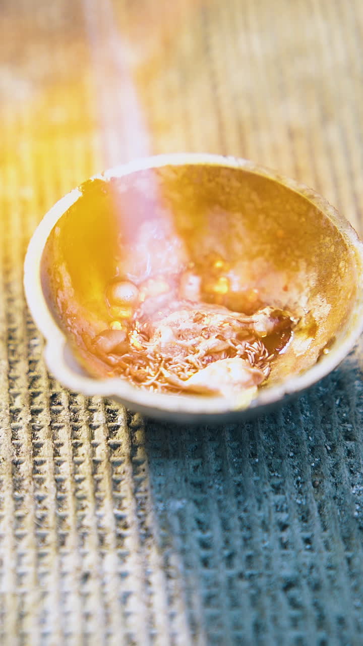 CU: melting pieces of gold metal in small crucible with flame on table with asbestos cover in jewelry workshop closeup