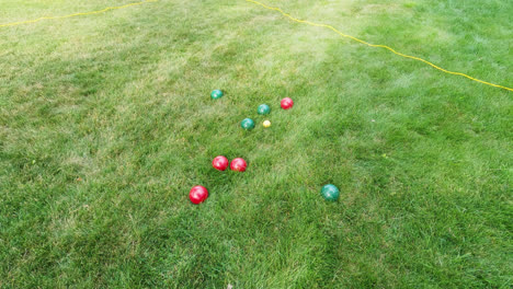 toma en ángulo alto de jugar al juego tradicional de petanca lanzando bolas rojas y verdes brillantes y pesadas al objetivo durante el día