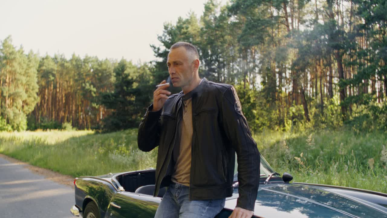 Man smoking by a classic convertible in the forest