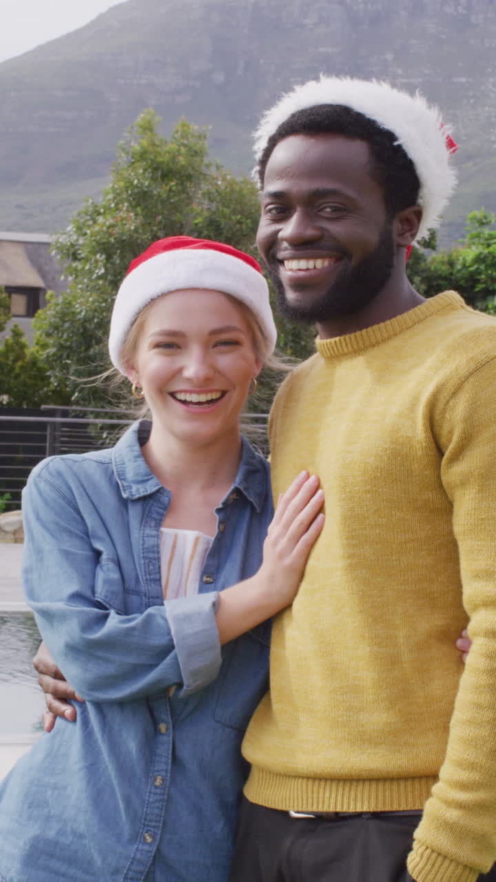 retrato vertical de video de una pareja feliz en sombreros de papá noel celebrando la navidad al aire libre