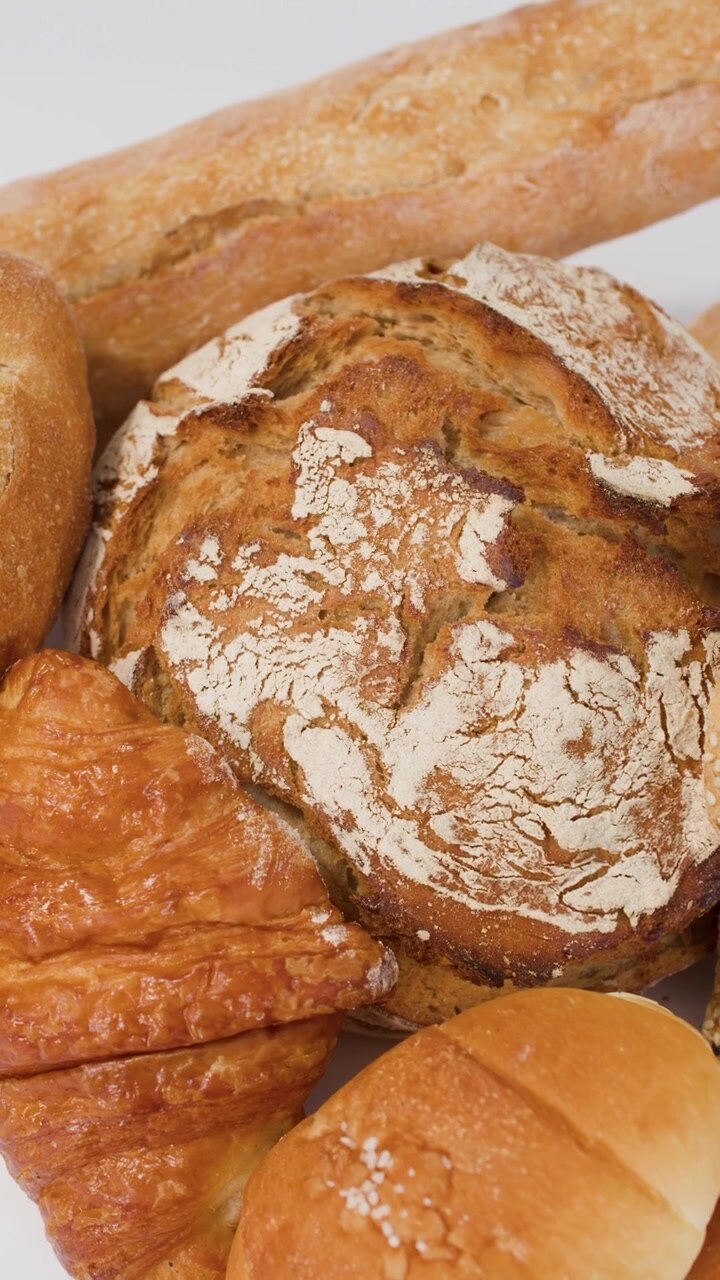 Slow camera pan across various artisan breads, croissants, and baguettes under bright studio lighting.