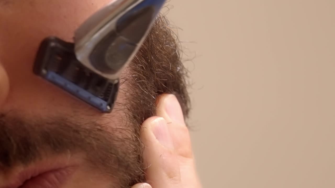 A detailed close-up of a bearded man shaving a part of his face, focusing on grooming and precision.