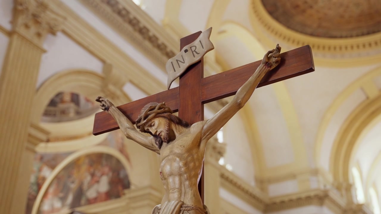 Dřevěná socha krucifixu Ježíše Krista uvnitř kostela. Pohled z nízkého úhlu na ukřižovanou postavu s nápisem INRI nahoře na rozmazaném pozadí náboženského interiéru v evropském kostele v Itálii.