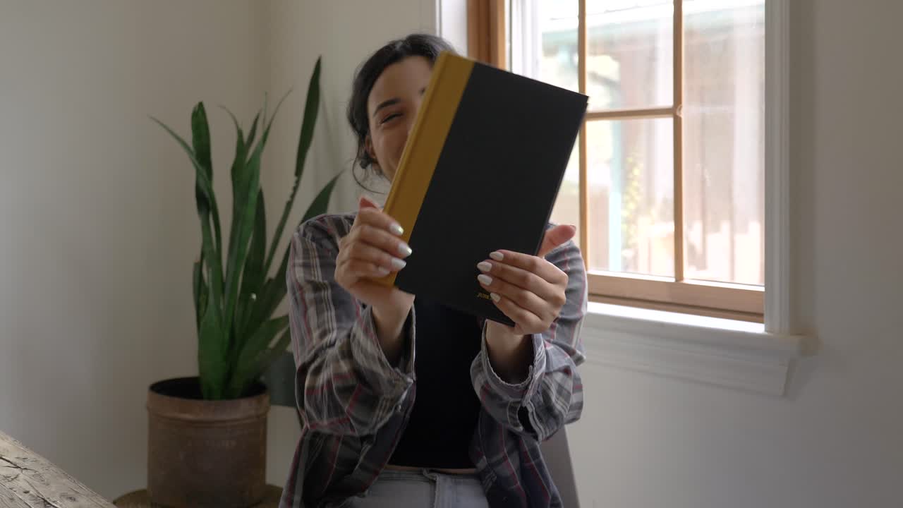 alegre chica puertorriqueña mirando a la cámara feliz sonriendo gratitud con nuevo libro de lectura