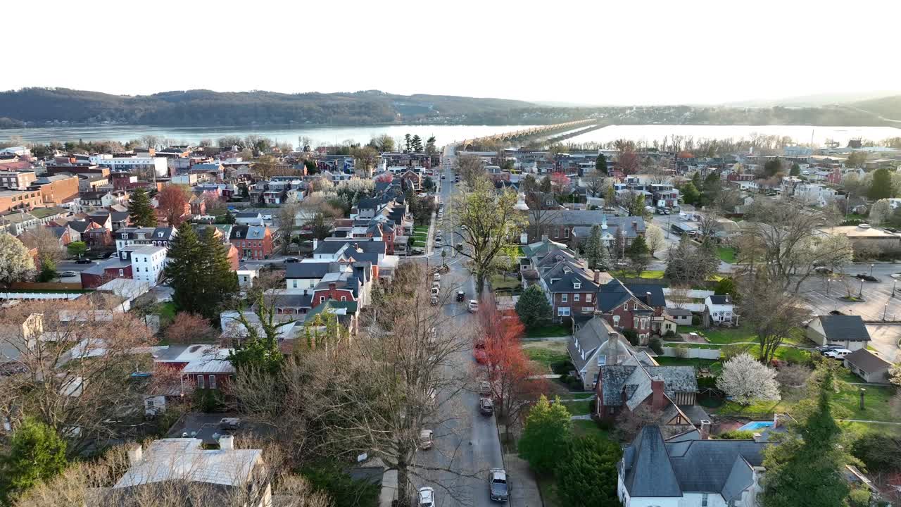 vista de avión no tripulado acercándose a una gran comunidad que se acerca a un puente sobre un hermoso río con colinas en el fondo al atardecer