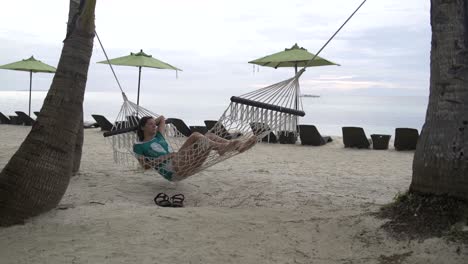 woman is lying in a hammock on the sea shore in the evening