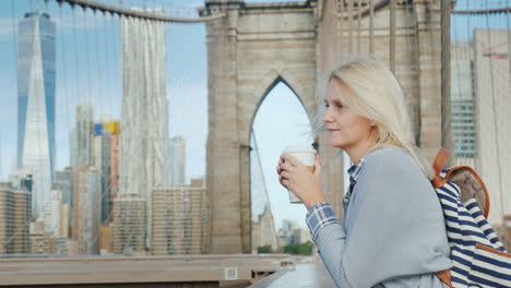 Eine-Frau-Mit-Einer-Tasse-Kaffee-In-Der-Hand-Steht-Auf-Der-Brooklyn-Bridge-Mit-Blick-Auf-Manhattan-S