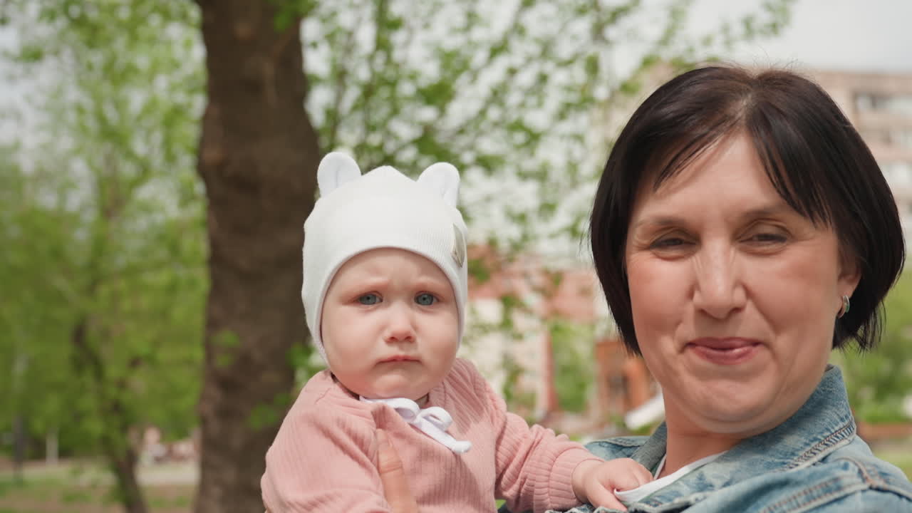 Grandmother With Baby, Senior Woman With Young Child Outdoors Amidst Lush Foliage And Warmth, Elderly Caucasian Grandmother Sharing Joyful Moment With Baby Amidst Springtime Park Scenery