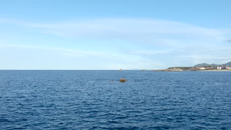 Sobrevuelo-De-Drones-Hacia-Una-Pequeña-Formación-Rocosa-Rodeada-De-Gaviotas,-Cabo-Quejo-En-Cantabria