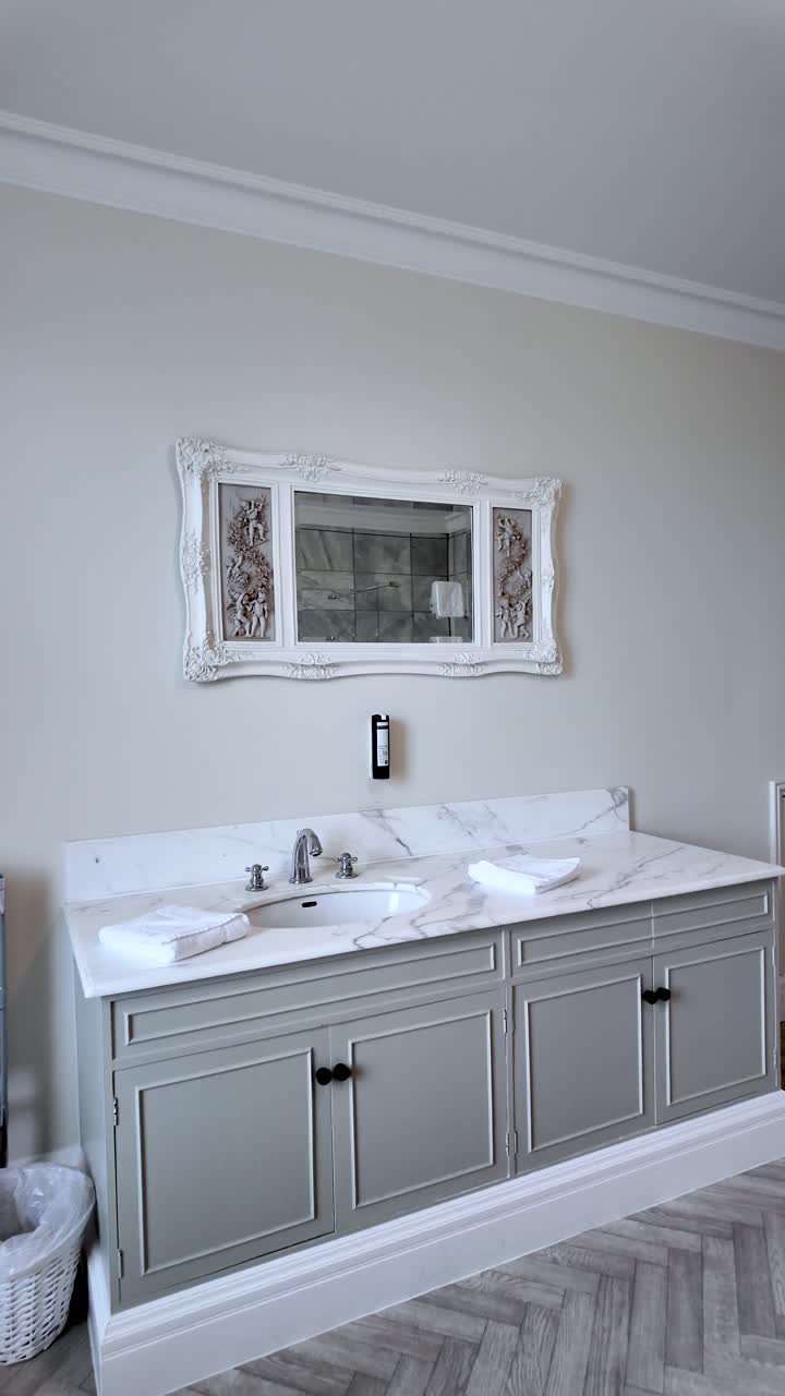 Mueble de baño con encimera de mármol, armarios grises, lavabo blanco, grifo, toallas y espejo ornamentado para proyectos de diseño de interiores y mejoras del hogar