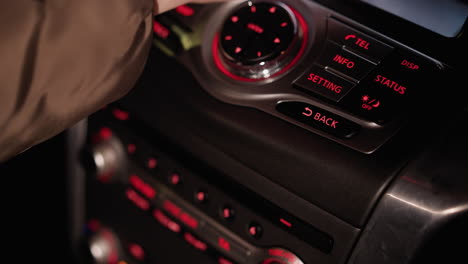 first-person view of a woman's hand pressing the settings button on a car control panel at night. the dashboard is illuminated with red lights, highlighting the controls. shot with a handheld camera