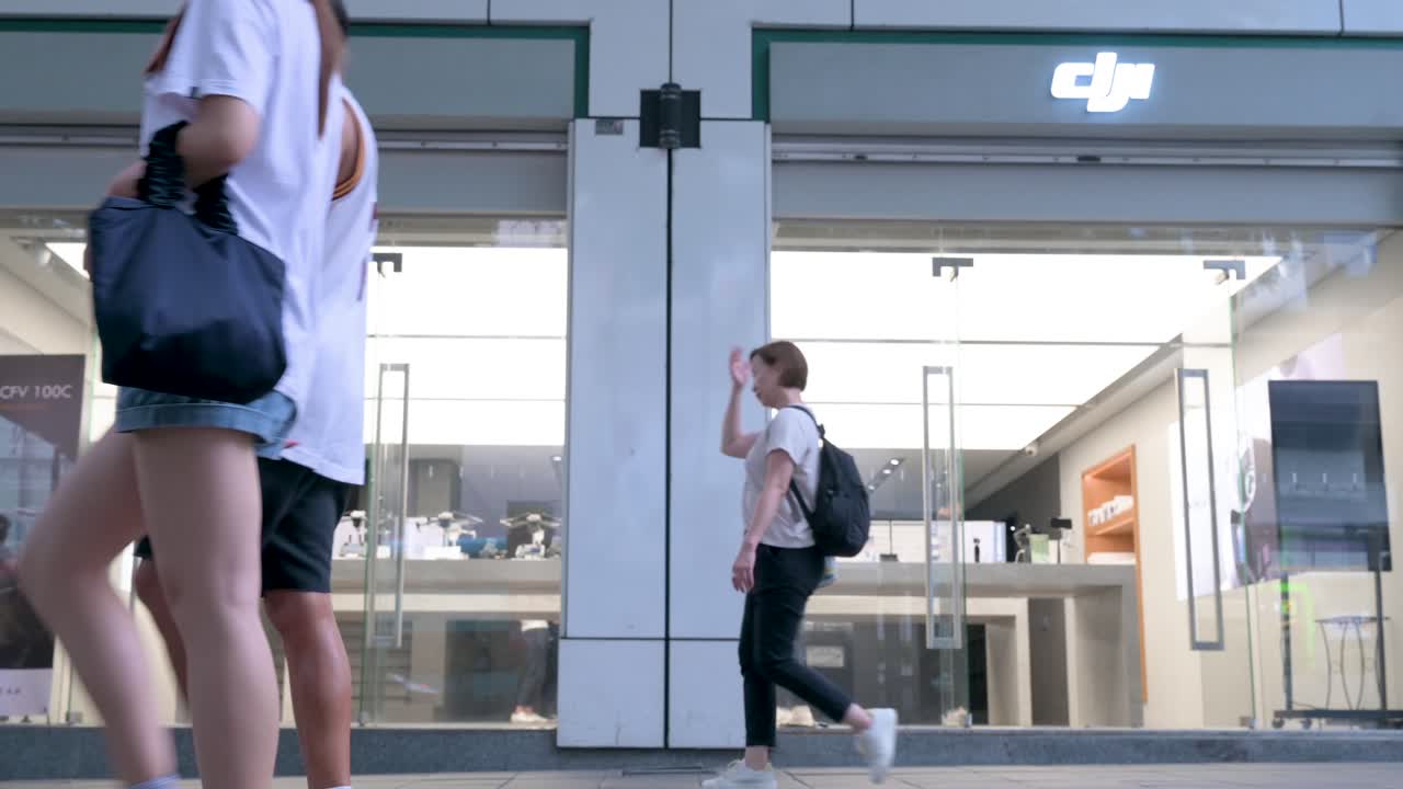 Low-angle view of pedestrians passing by DJI's official store in Hong Kong, where the Chinese technology company, renowned for its drones and camera gear, attracts customers.