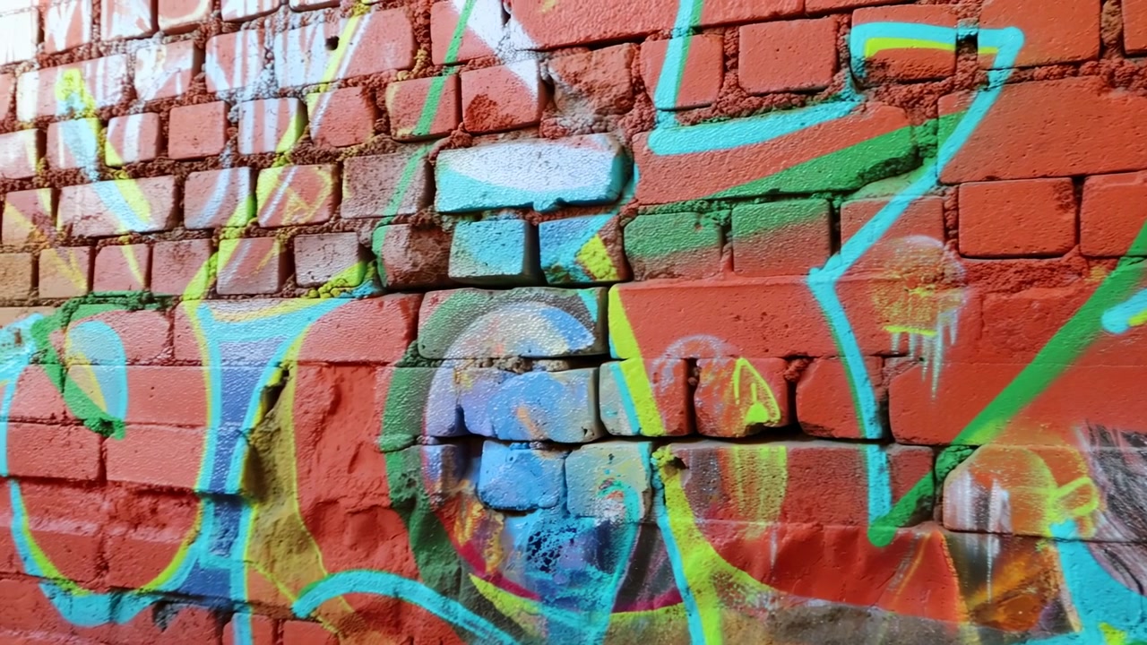 Graffiti colorati su muro di mattoni rossi, vivace arte di strada con contorni al neon e colature di vernice spray, testurizzato.