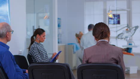 Back-view-of-patient-filling-in-dental-form-sitting-on-chiar