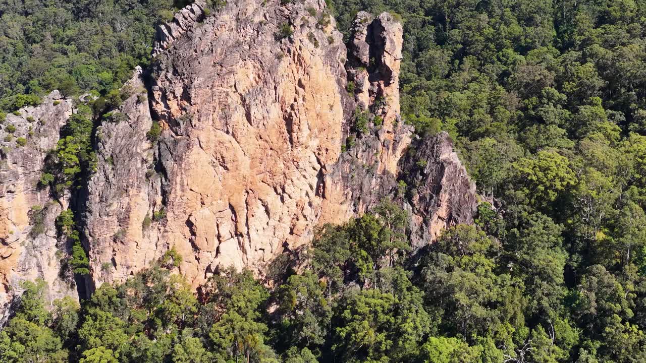 Drone footage captures Nimbin Rocks surrounded by dense forest under bright daylight, showcasing natural beauty and geological formations